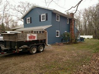 Blue vinyl siding job with the City Roofing & Siding trailer in the driveway