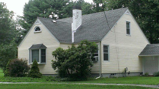 Cream-sided Cape Cod with a new gray shingle roof and chimney