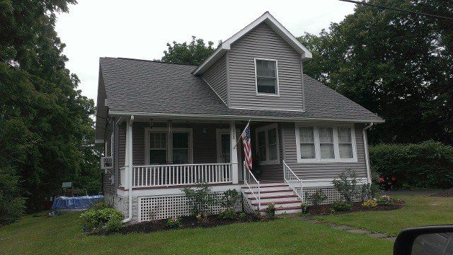 Side view of a Cape Cod home with a new gray shingle roof and dormer